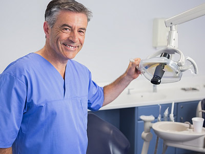 Ein Zahnarzt in blauer Arbeitskleidung lächelt und hält ein zahnärztliches Instrument.